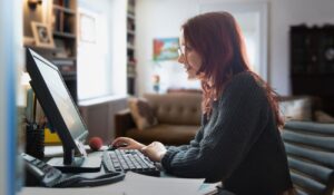Mujer concentrada trabajando en un ordenador de escritorio en una sala iluminada por la luz del día