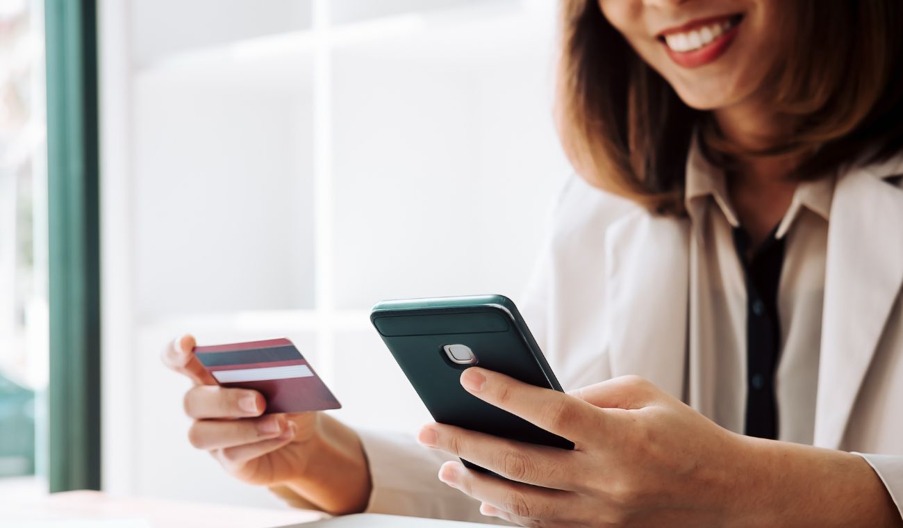 Persona sonriendo sostiene un teléfono móvil y una tarjeta de crédito