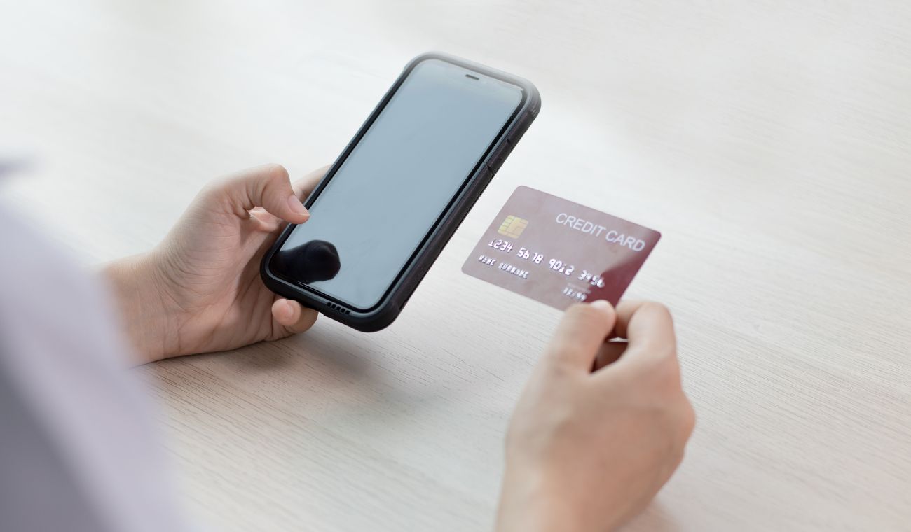Persona sosteniendo un teléfono móvil y una tarjeta de crédito sobre una mesa