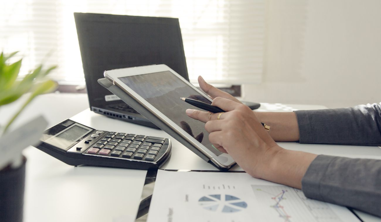 Persona usando tablet con gráficos en oficina junto a calculadora y portátil